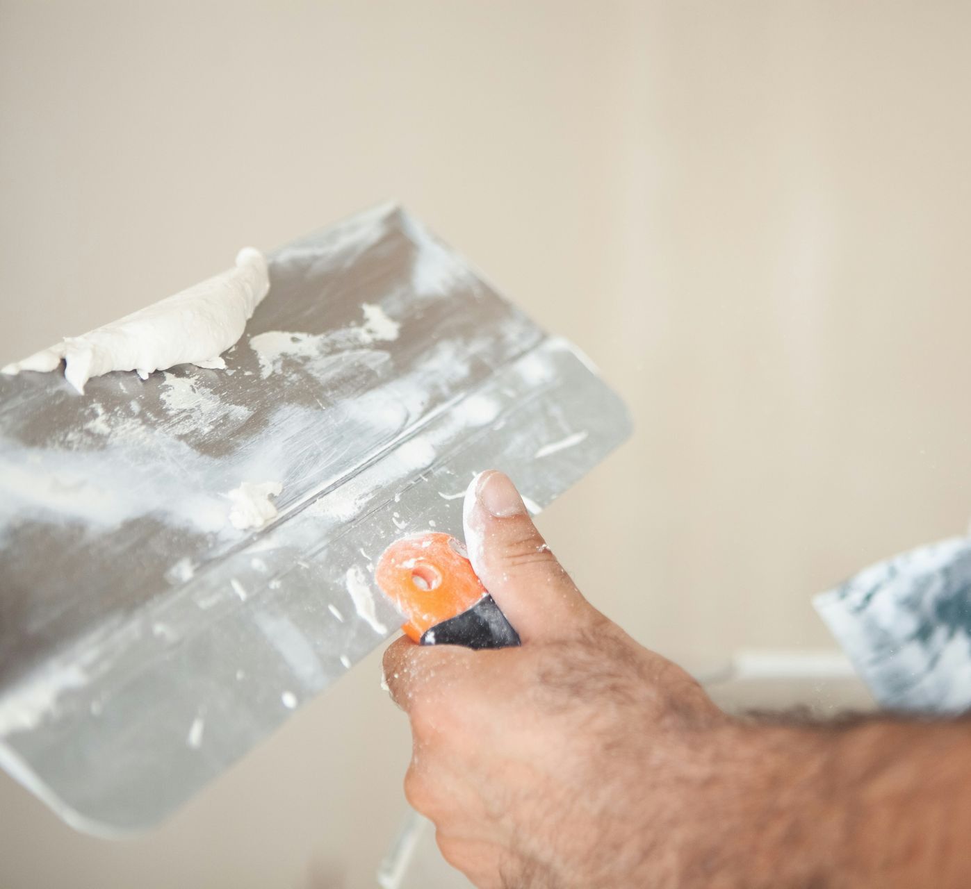 Hands applying plaster to a wall with trowels