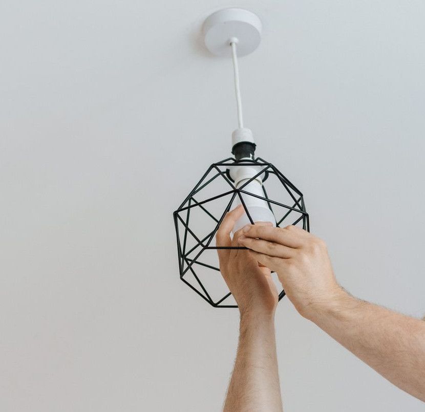 From below of male screwing light bulb into new fashionable lamp during renovation work in apartment